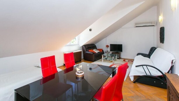 Ein modernes Loft mit hohen Decken, einem Essbereich mit Glastisch, roten Stühlen, einer schwarzen Couch, einem weißen Sessel und einem Fernseher.