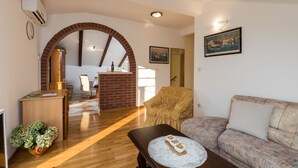 A spacious living area with a wooden floor, a sofa, a dining table, and a brick fireplace.