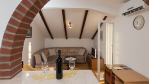 A cozy living room with a curved brick archway, a sofa, a dining table with a wine bottle and glass, and a clock on the wall.