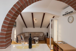 Una sala de estar acogedora con un arco de ladrillo, un sofá, una mesa de comedor con una botella de vino y una copa, y un televisor sobre un mueble de madera.