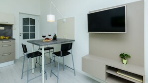 A modern kitchen with a dining table, chairs, a TV mounted on the wall, and a small potted plant. - Villa Panorama Dubrovnik - Comfort One Bedroom Apartment with Balcony and sea View (Mlini)