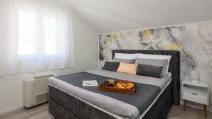 A modern bedroom with a large bed, a bedside table, a heater, and a wall with abstract art. - Villa Panorama Dubrovnik - Comfort One Bedroom Apartment with Balcony and sea View (Mlini)