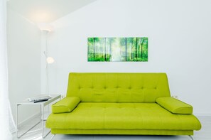 A bright green sofa with a remote control on a white table beside it.