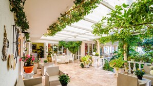 Un espacio de patio cubierto con mobiliario de mimbre, plantas en macetas y vistas al interior.