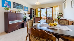 A dining area with a wooden table, chairs, and a cabinet. There are paintings on the wall and a window with curtains.