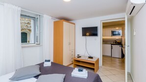 Ein Hotelzimmer mit Bett, Schreibtisch, Fernseher und einer kleinen Küchenzeile im Hintergrund.