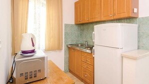 A compact kitchen with wooden cabinets, a sink, a white refrigerator, and a kettle on a small table. - Apartments Čiovo - Comfort One Bedroom Apartment with Terrace (Okrug Gornji)