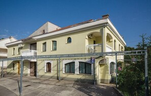 A two-story building with a balcony on the second floor, a covered entrance, and a small garden area.
