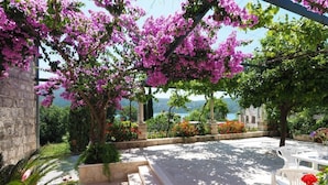 An outdoor patio with a pergola covered in pink flowers, stone walls, and a view of the sea. - Apartments & Room Eva Slano- Double Room with Balcony and Sea View (Slano)