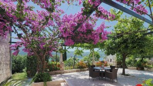 An outdoor patio with a table and chairs, surrounded by lush greenery and flowering plants. - Apartments & Room Eva Slano- Double Room with Balcony and Sea View (Slano)
