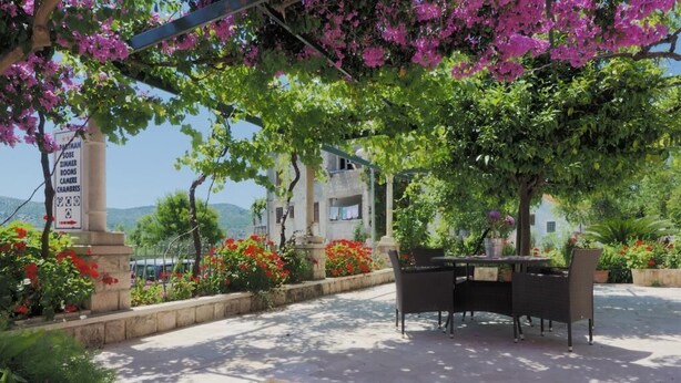 An outdoor seating area with a table and chairs, surrounded by flowering plants and a pergola with pink flowers. - Apartments & Room Eva Slano- Double Room with Balcony and Sea View (Slano)