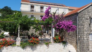 A building with a stone facade, a balcony, and a garden with purple flowers. - Apartments & Room Eva Slano- Double Room with Balcony and Sea View (Slano)