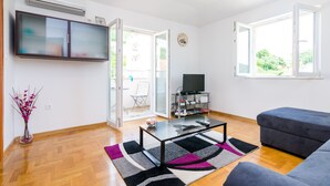 En moderne stue med et fladskærms-tv, et glasbord, en grå sofa og et stort vindue.