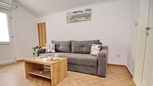 A living room with a grey sofa, wooden coffee table, and a painting of boats on the wall. - Apartments Memunić - Standard One Bedroom Apartment with Partial Sea View (Ston)