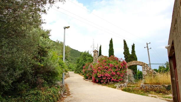 A rural road with a stone archway, surrounded by greenery and a stone building. - Apartments Memunić - Standard One Bedroom Apartment with Partial Sea View (Ston)