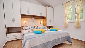 A bedroom with a bed, white cabinets, a window with curtains, and a wall-mounted light. - Apartments Memunić - Standard One Bedroom Apartment with Partial Sea View (Ston)