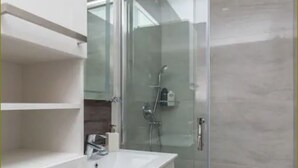 Un bagno moderno con cabina doccia in vetro, lavabo bianco e specchio.