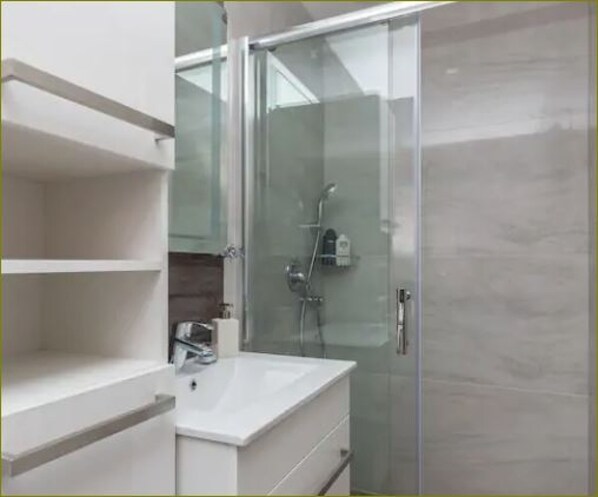 Une salle de bain moderne avec une douche à parois de verre, un lavabo blanc et un miroir.