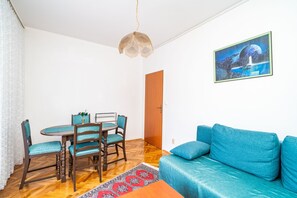 A room with a blue sofa, a dining table with chairs, a hanging light fixture, and a painting on the wall.