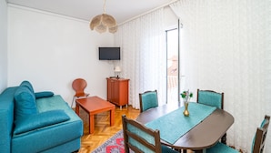 A living room with a sofa, a dining table with chairs, a TV, and a cabinet. - Apartments Peco - Four Bedroom Apartment with Balcony and Sea View (Mokosica)