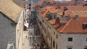 Una calle histórica con una torre destacada y edificios con tejas rojas.