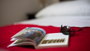 Una cama con un abrigo rojo, un libro y un par de gafas de sol encima.