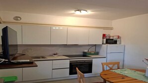 Una cocina compacta con armarios blancos, microondas, refrigerador y una mesa de comedor con sillas.