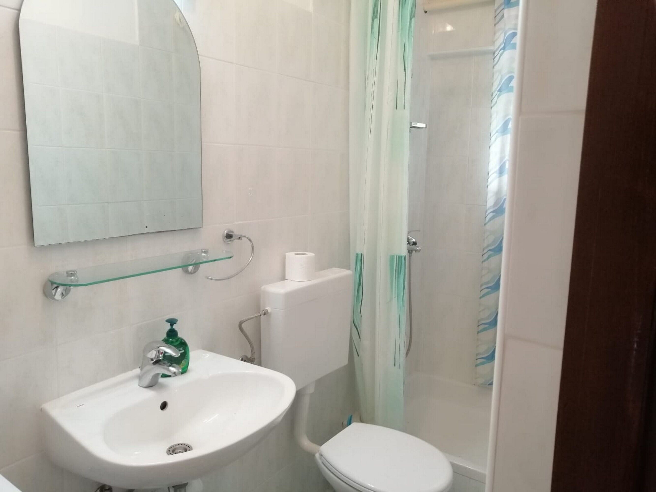 Une salle de bain avec un lavabo, des toilettes et une douche, le tout de couleur blanche.