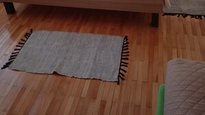 Una cama con colchón blanco, dos almohadas y una almohada de color amarillo. Hay dos mesitas de noche con lámparas, una alfombra gris y suelo de madera.