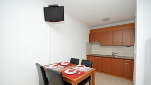 A compact kitchen with wooden cabinets and a tiled backsplash. A dining table with chairs is set for four, with plates and cutlery.