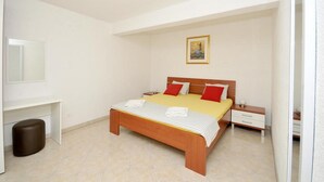 A bedroom with a bed, nightstands, a small table, a trash bin, and a painting on the wall.
