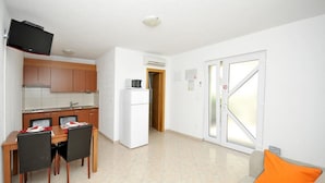 A compact living space with a kitchenette, dining area, and a sofa with an orange cushion.