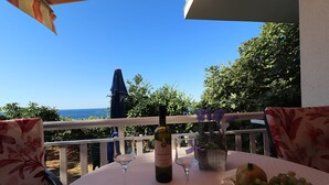 Une table avec une bouteille de vin, deux verres à vin et un bol de raisins, le tout placé sur un balcon donnant sur la mer.
