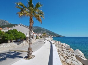 A coastal street with a palm tree, stone buildings, and a clear blue sea. - Dva Galeba - One Bedroom Apartment with Sea View (204) (Bol)
