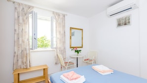 A hotel room with a bed, a small table, two chairs, a mirror, and an air conditioning unit.