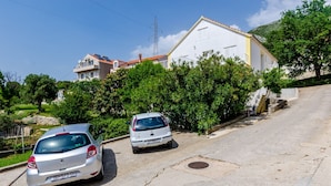 A residential street with two parked cars, a white building with a red roof, and lush greenery.