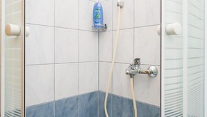 Een douche met een handdouche, een shampoo fles en een douchecabine met glazen wanden.