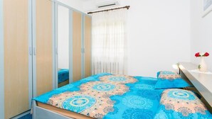 Een slaapkamer met een bed, een kledingkast, een spiegel, een raam met gordijnen en een nachtkastje met een bloemenvaas.