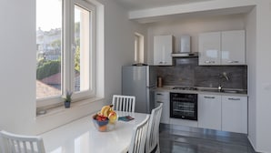 Une cuisine moderne avec des meubles blancs, un four encastré et une fenêtre donnant sur un quartier résidentiel.