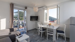 Un salon moderne comprenant un canapé, une table à manger avec des chaises, un téléviseur à écran plat et une grande fenêtre donnant sur un paysage vallonné.