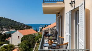 Un balcon avec une table et des chaises, offrant une vue sur la côte, avec des bâtiments et des arbres.