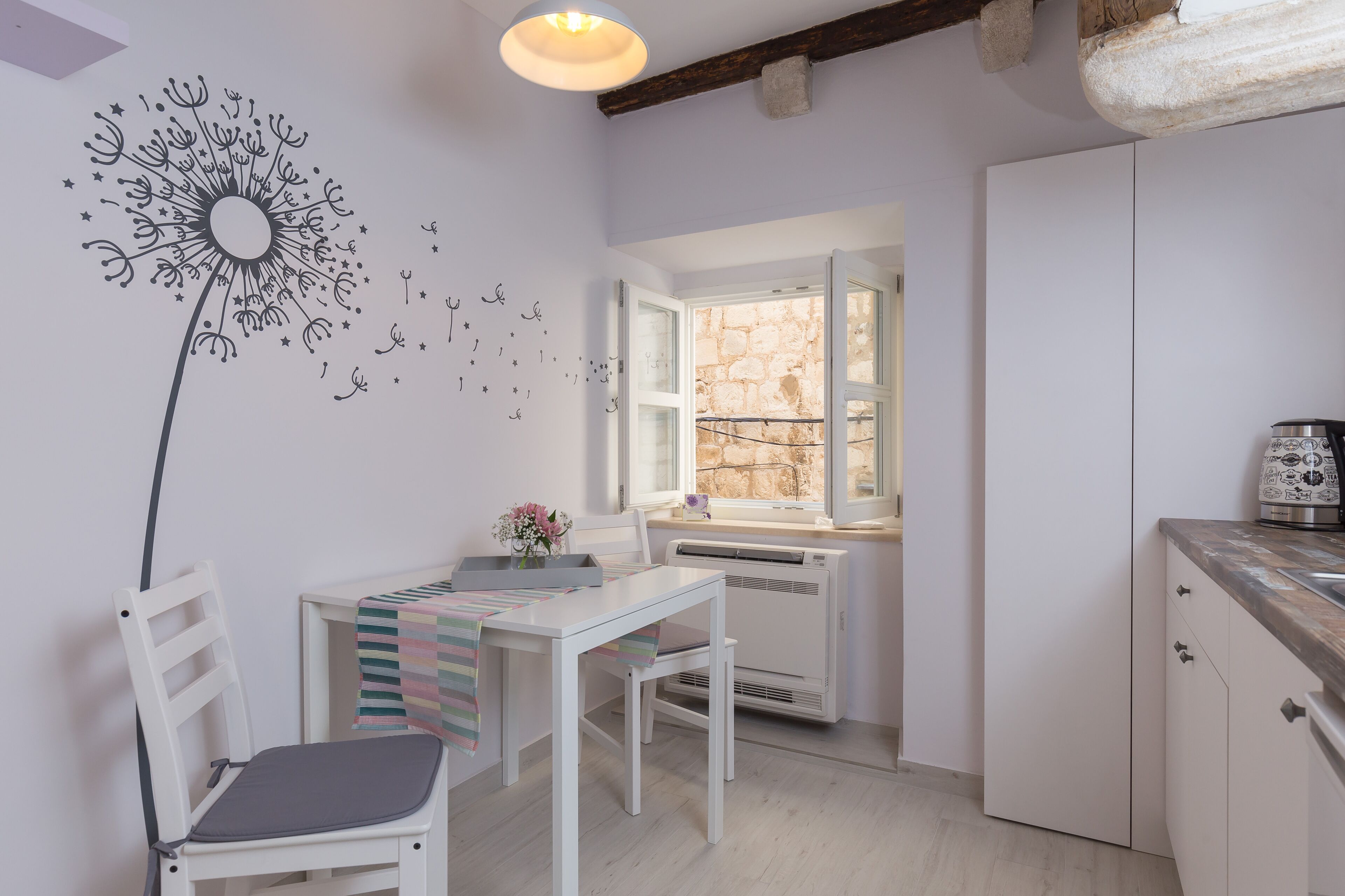 Una cocina moderna con una mesa blanca, sillas y una ventana con vistas a una pared de piedra.