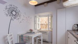 A kitchen with a white table, a chair, a dandelion wall art, a window, and a stone wall.