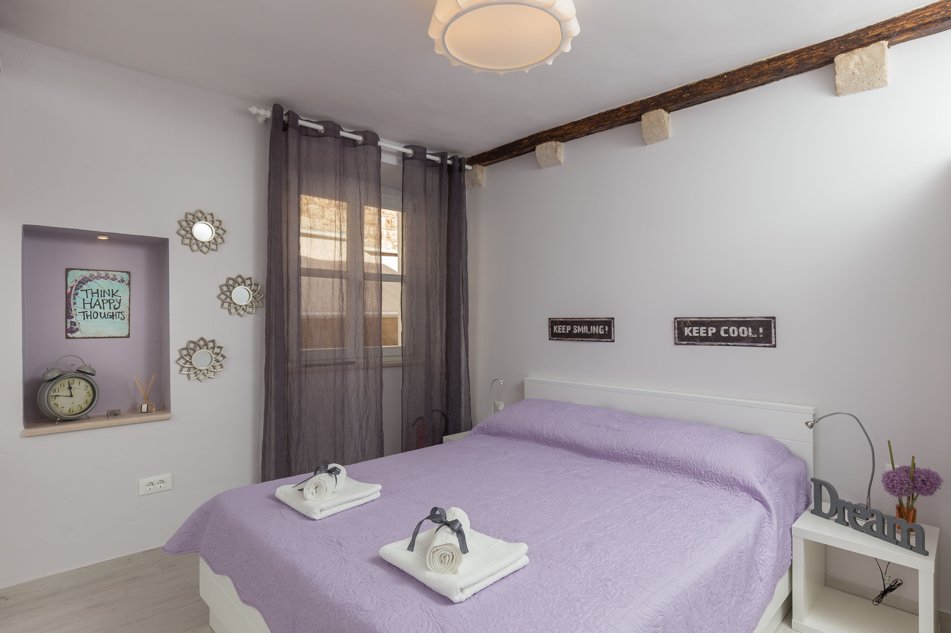 A bedroom with a bed, two towels, a clock, and motivational signs on the wall.