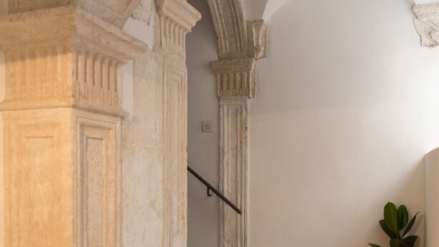 A hallway with a stone floor, a potted plant, and a staircase with a handrail.