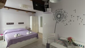 A bedroom with a bed, a desk, a chair, a TV, and a wall decoration.