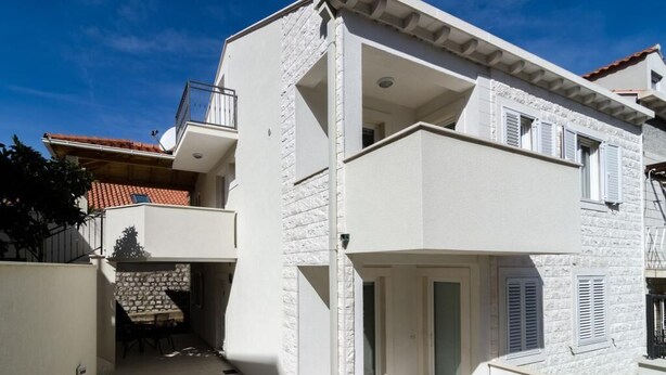 Ein zweistöckiges Gebäude mit einem Balkon im oberen Geschoss, einer kleinen Außen-Sitzgelegenheit und einer Steinfassade.