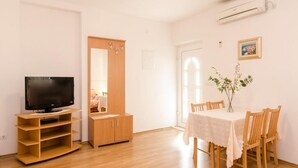 Ein Zimmer mit Fernseher auf einem Holzboden, einem Esstisch mit Stühlen, einem Holzschrank und einer Klimaanlage an der Wand.