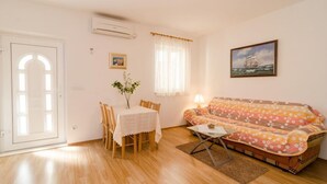 Ein Wohnzimmer mit Holzboden, einem Esstisch mit Stühlen, einer Couch, einer Lampe und einem Bild an der Wand.