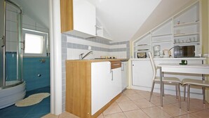 A compact kitchen with a central island, a dining area with a table and chairs, and a shower area with a glass door. - Apartments Villa Rose - Standard Studio with Sea View Terrace (A2 bijeli) (Sumartin)